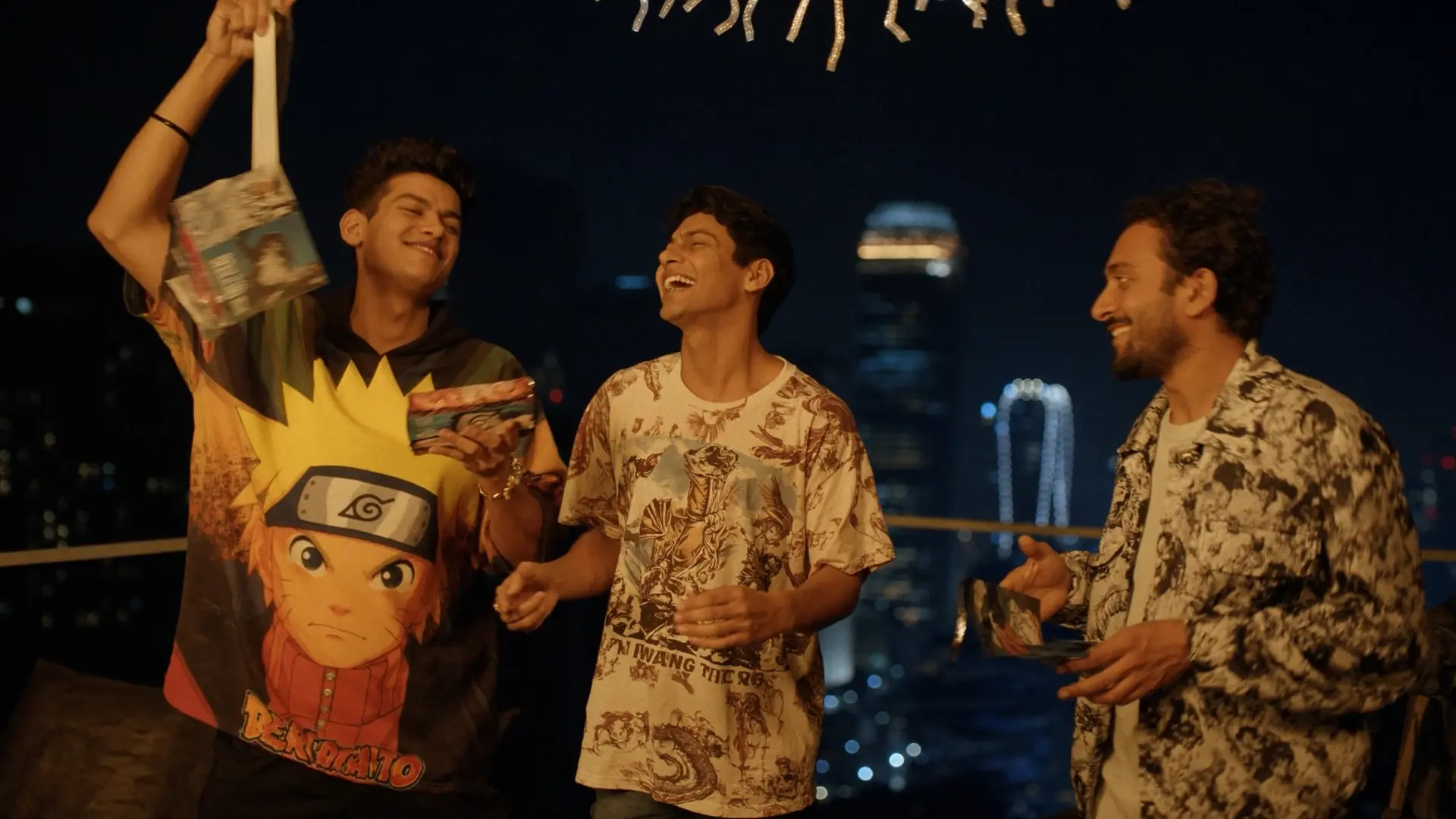 Group of young Indian friends wearing anime graphic streetwear at a night rooftop event in India, celebrating and laughing