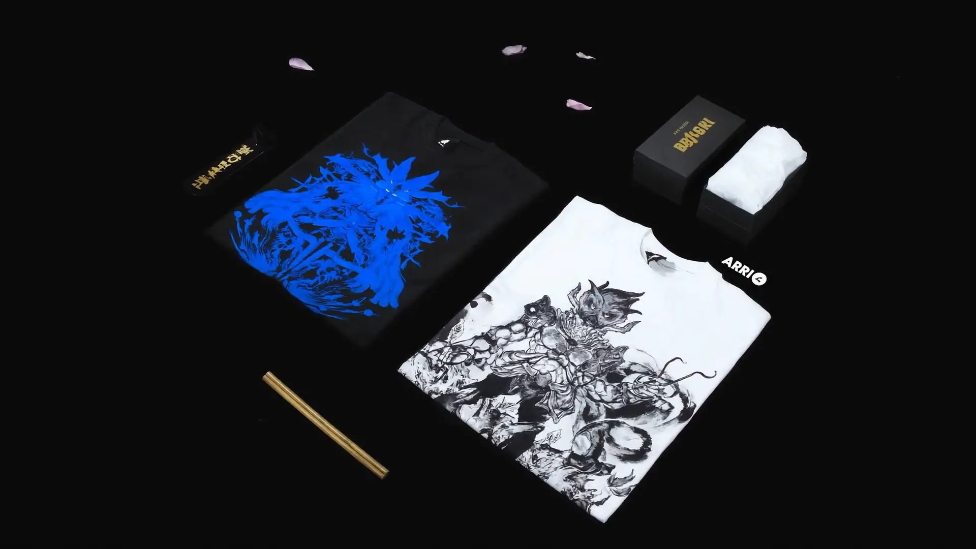 Premium anime streetwear brand product flat lay with folded anime graphic tshirts, branded packaging, custom tags and stickers on dark matte surface