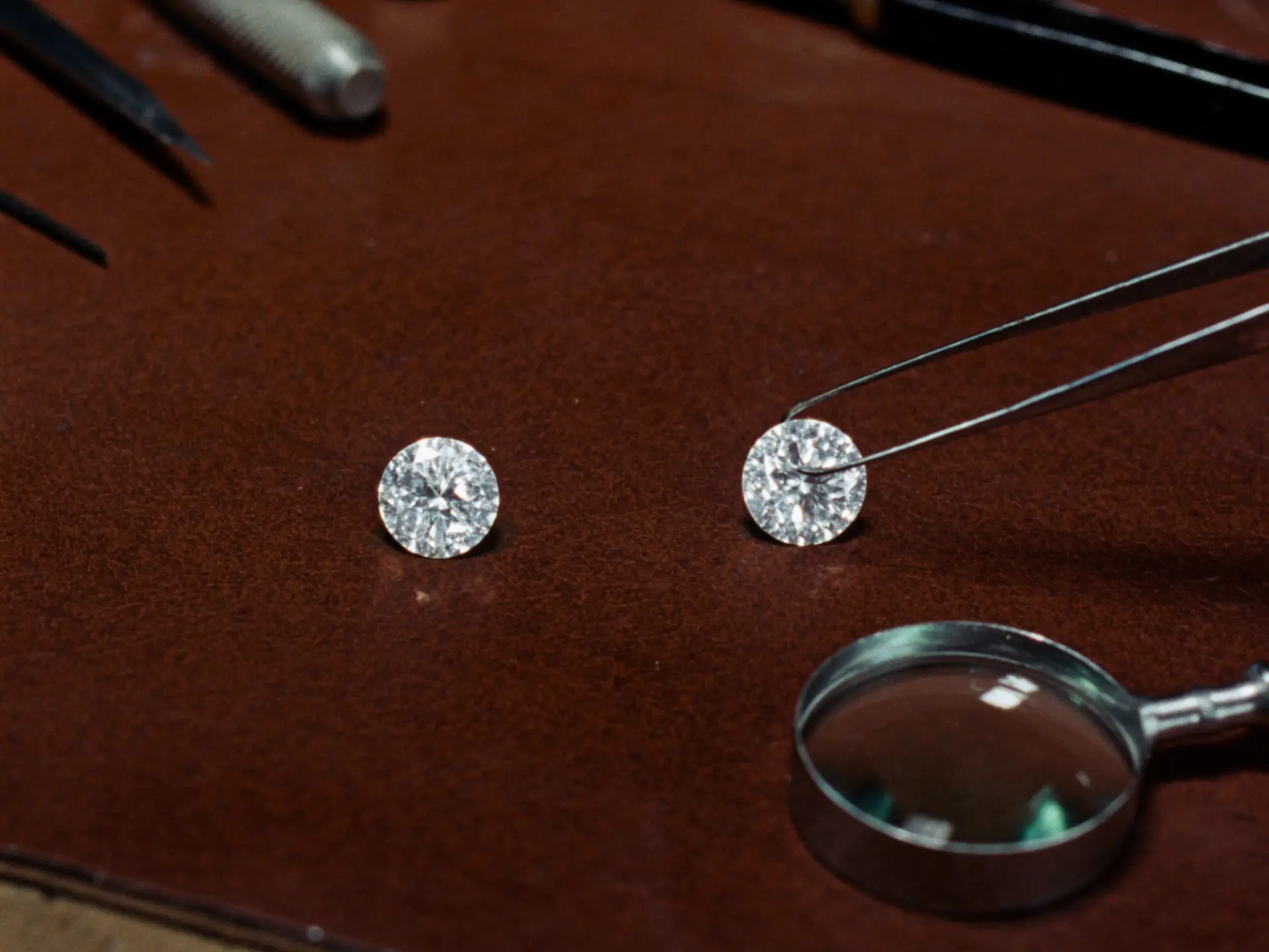 Two identical round brilliant diamonds compared side by side with tweezers and loupe on a jeweller's bench in Surat